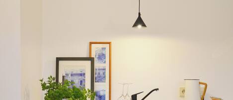 A modern kitchen with a grey cabinet, a hanging pendant light, a potted plant, framed pictures, and a towel on the counter.