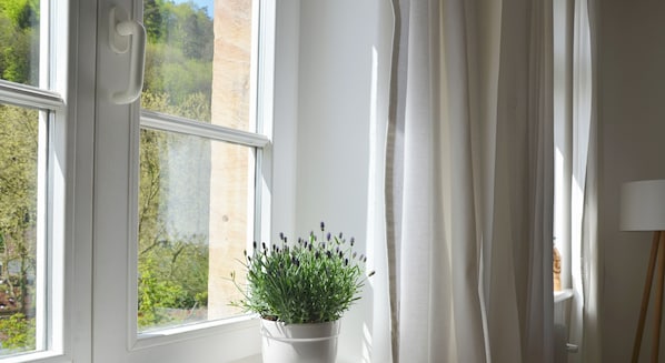 Una ventana con una maceta de lavanda, un radiador y una lámpara en el alféizar.