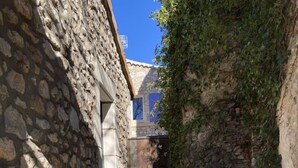 A narrow outdoor corridor with stone walls, a tiled floor, and metal chairs.