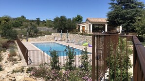 A pool area with a stone wall, a wooden deck, and a house in the background.