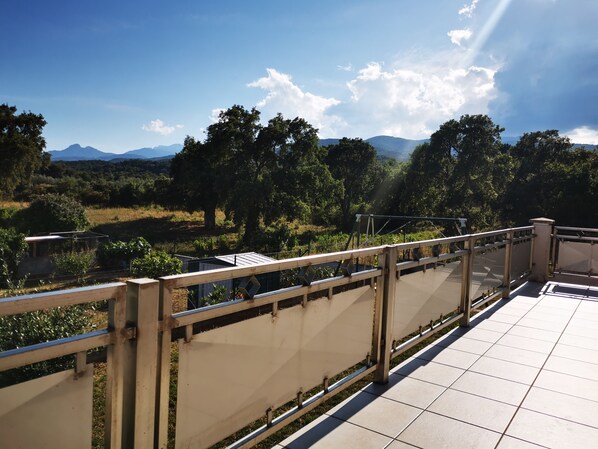 Eine Terrasse mit Blick auf eine gebirgige Landschaft, einem Metallgeländer und gefliestem Boden.
