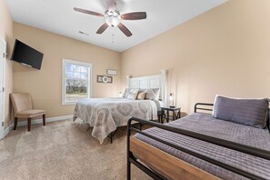 Une chambre avec un lit, une chaise, un téléviseur, un ventilateur de plafond et une fenêtre.