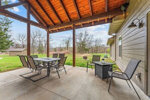 Une terrasse extérieure dotée d’une pergola en bois, d’une table avec des chaises et offrant une vue sur une maison et un jardin.