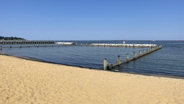 Una playa arenosa con un muelle de madera que se adentra en aguas tranquilas.
