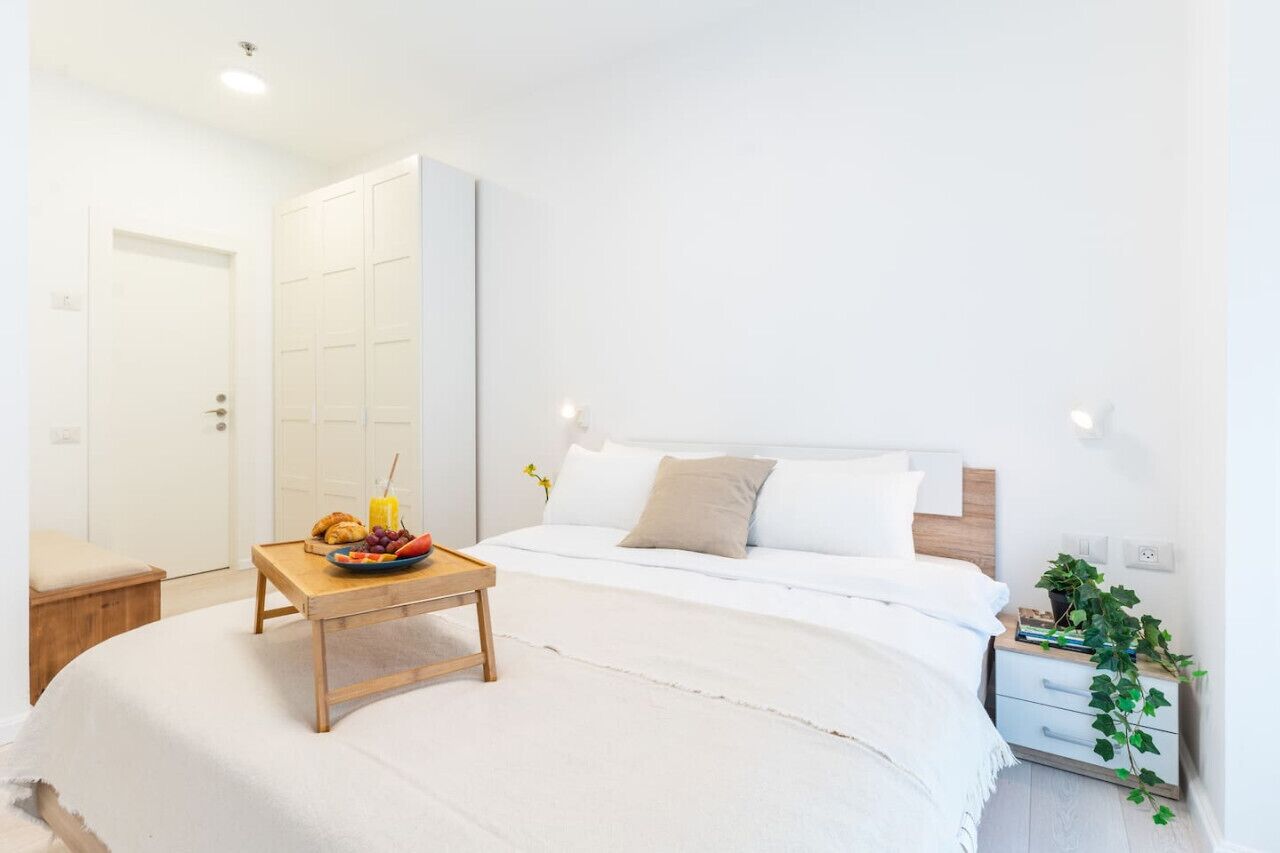 Un dormitorio con cama, mesita de noche y un velador con una planta.