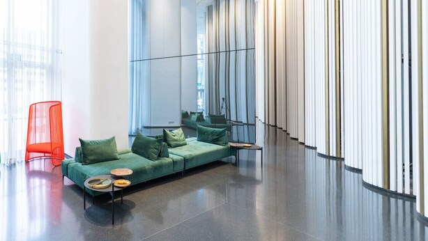 Eine moderne Lobby mit einem grünen Sofa, einem roten Sessel und einer Glastrennwand.