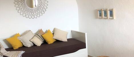 Una sala de estar moderna con un sofá blanco, un espejo redondo, una lámpara colgante de mimbre y una pequeña mesa blanca.
