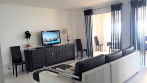 Un salon moderne avec un canapé, un téléviseur et un coin repas équipé de chaises.