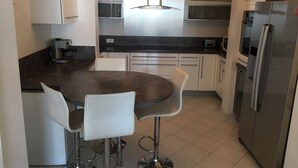 Une cuisine moderne dotée d’un plan de travail foncé, de tabourets de bar blancs, d’appareils électroménagers en acier inoxydable et d’un îlot central.