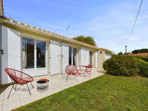Un bâtiment à deux étages doté d’une terrasse carrelée, de chaises rouges et d’une petite table.