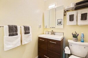 A bathroom with two towels hanging on a rack, a sink with a mirror above it, and a toilet with a potted plant beside it. - Perfect Private Getaway in Seattle's Southside! (SeaTac)