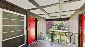 Un ingresso coperto con una porta rossa con il numero '206', una porta in vetro e vista su un giardino curato.