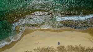 An aerial view of a beach with waves crashing onto the shore and a person standing in the water. - Villa Lantana - Salinus Naxian Villas (Naxos)