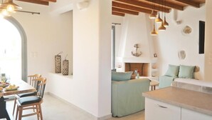 A modern kitchen with wooden beams, a dining area with chairs, and a cozy seating area with cushions. - Villa Lantana - Salinus Naxian Villas (Naxos)