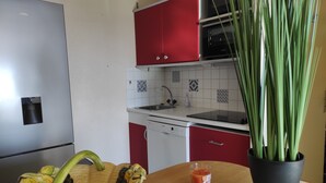 Ett kök med röda skåp, ett kylskåp i rostfritt stål, en diskmaskin och en krukväxt.
