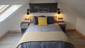 Een slaapkamer met een bed, twee nachtkastjes, een raam en een stadsgezicht schilderij aan de muur.