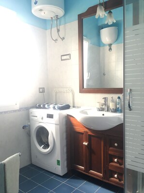 Une petite salle de bain équipée d’un lave-linge, d’un lavabo et d’un miroir.