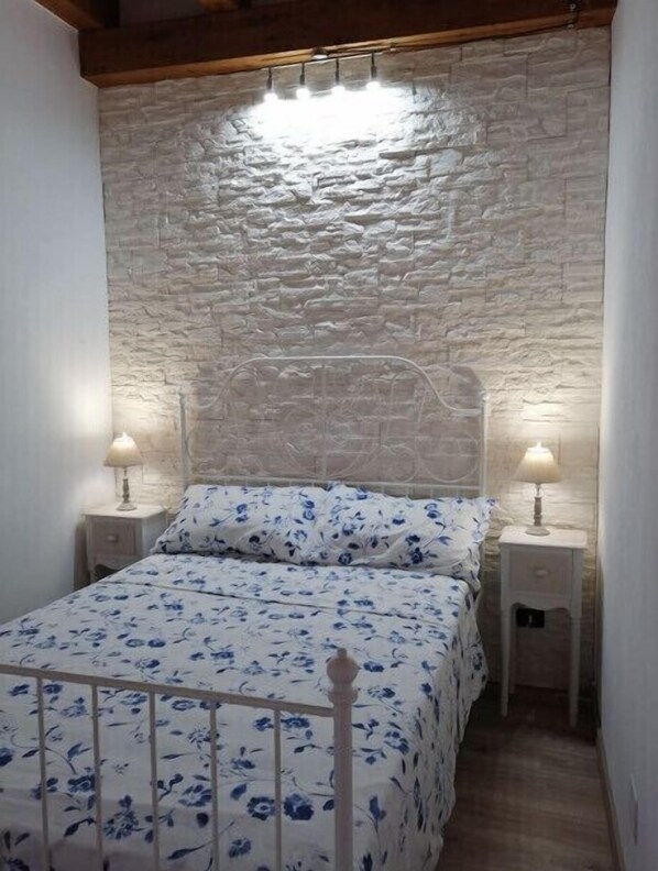 Une chambre avec un mur en pierre, un lit recouvert d’une literie à motifs floraux et deux lampes de chevet.