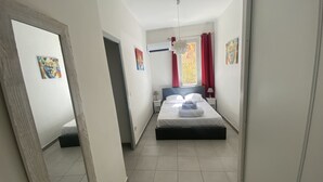 Une chambre d’hôtel avec un lit, une table de chevet, une lampe, une fenêtre avec des rideaux rouges et un ventilateur de plafond.