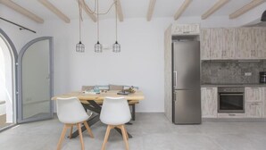 Una cocina moderna con vigas de madera, un refrigerador de acero inoxidable y un comedor con mesa de madera y sillas blancas.