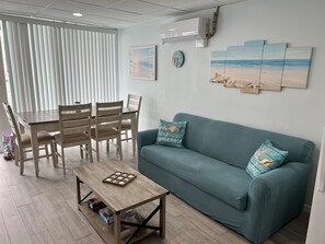 A living room with a wooden dining table, teal sofa, and artwork on the walls. - Family-Friendly Getaway, Steps from Beach! (Wildwood Crest)