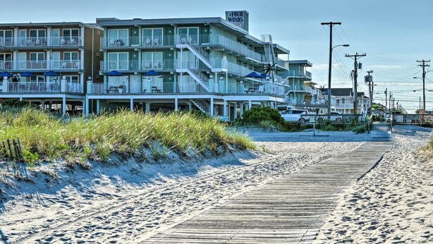 Un hotel frente al mar con varios balcones, un paseo marítimo de madera y una playa arenosa.