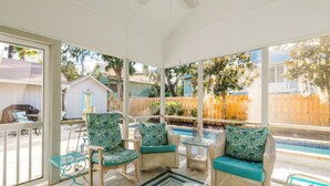 A sunroom with wicker furniture, a glass table, and a view of a backyard with a pool. - 14 Egret - Easy Sea, Near Beach and Coligny (Hilton Head Island)