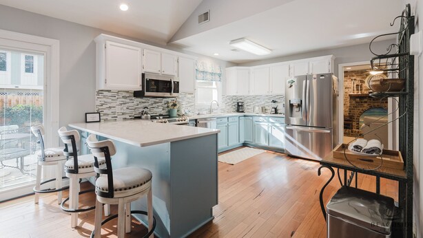 A modern kitchen with white cabinets, a central island with bar stools, a stainless steel refrigerator, and a brick accent wall. - 14 Egret - Easy Sea, Near Beach and Coligny (Hilton Head Island)