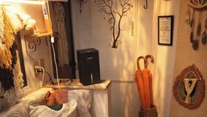 Een gezellige woonkamer met een bank, een bijzettafeltje met bloemen, een wandklok en decoratieve items, waaronder een dreamcatcher en een ingelijste foto.