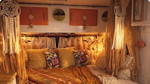 Een gezellig bed met een deken met patroon, bloemenkussens en een dreamcatcher erboven.