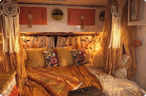 A cozy bed with a patterned blanket, floral pillows, and a dreamcatcher hanging above.