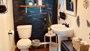 Een badkamer met een zwarte wand, witte sanitair, een houten vloer, een hangende lamp en een raam.