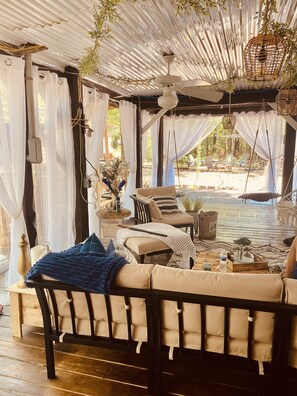 A cozy outdoor seating area with a sofa and chairs, a small table with drinks, and a view of the garden.