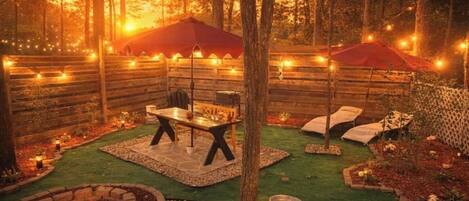 A cozy outdoor patio area with a table and chairs, surrounded by a wooden fence and string lights.