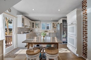 A modern kitchen with white cabinetry, a stainless steel island, and a brick accent wall.
