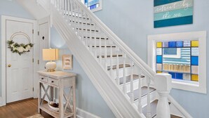 A staircase with white balusters, a wall with a blue and white sign, and a window with colorful stained glass. - Peach Perfect Victorian Home with Gourmet Kitchen (Cape Charles)