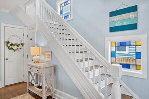 A staircase with white balusters, a wall with a blue and white sign, and a window with colorful stained glass.