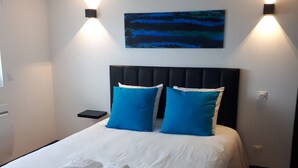 Ein ordentlich gemachtes Bett mit weißen Leinentüchern und zwei blauen Kissen, ein schwarzer Kopfteil und ein Gemälde darüber.