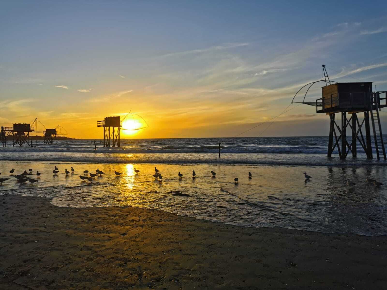 A beach at sunset with a lifeguard tower and a pier.