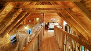 Un interior de madera con una escalera central, barandillas de madera y una cama con ropa blanca.