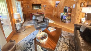 Interior acogedor de una cabaña de troncos, con un sofá de cuero, una mesa de centro de madera y un televisor en la pared.