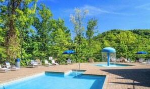Ein Swimmingpool mit Liegestühlen und Sonnenschirmen, umgeben von Bäumen.