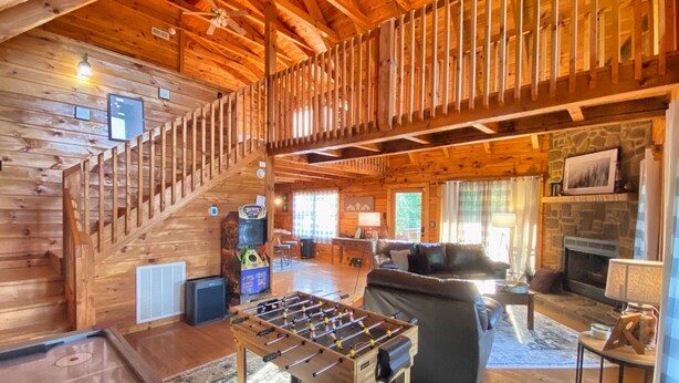 Acogedor interior de cabaña de madera con mesa de fútbol, chimenea, sofá y escalera.