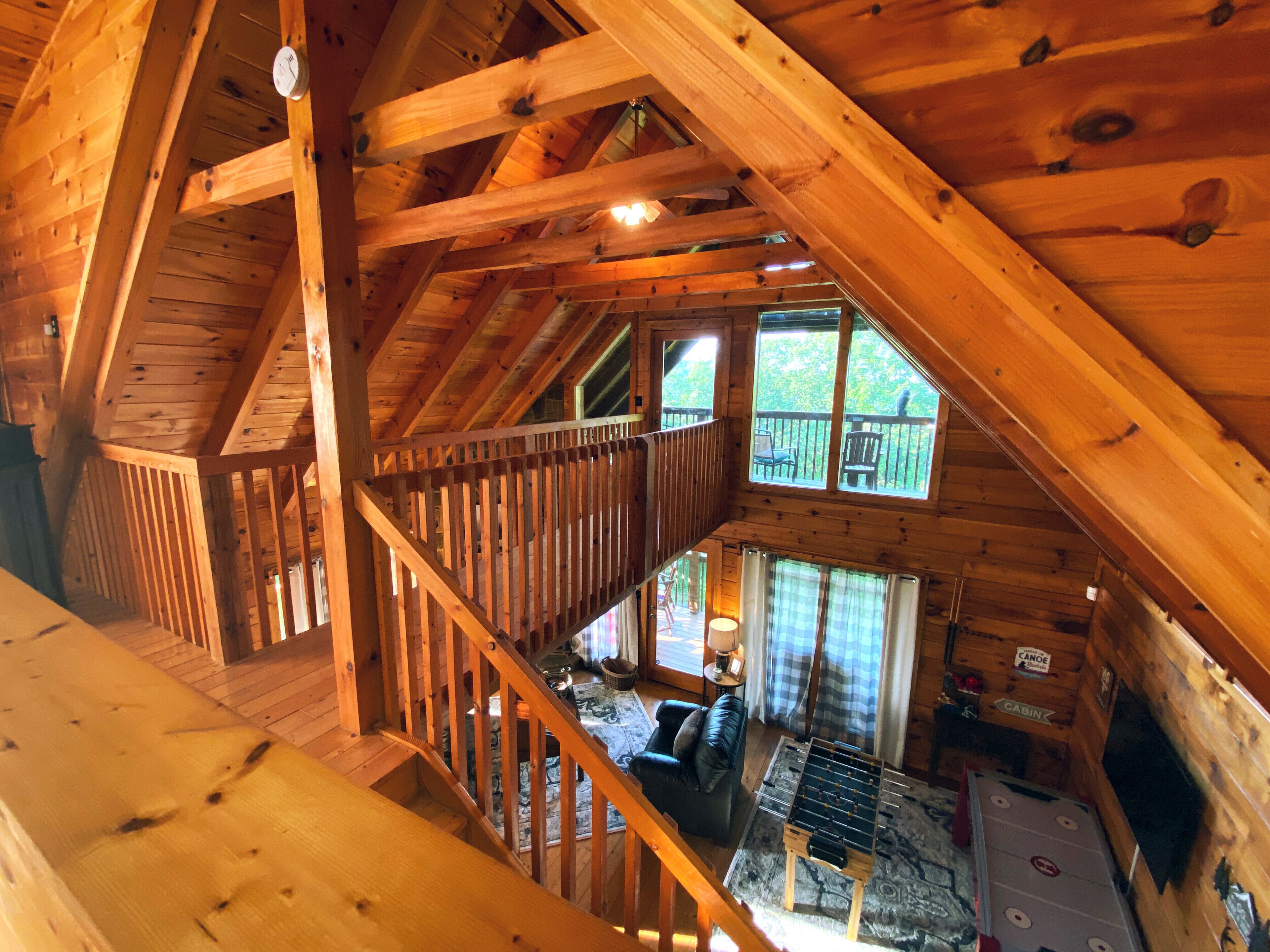 Una cabaña de madera con habitación en entrepiso, sala de estar con mesa de fútbol y balcón con mobiliario exterior.