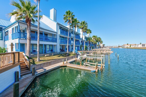 A waterfront hotel with balconies, a dock, and palm trees.
