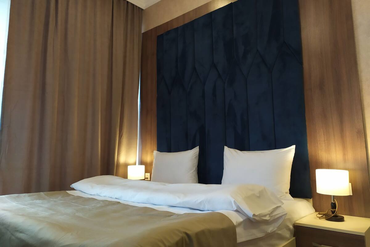 A hotel room with a large bed, two bedside lamps, and a wooden headboard.
