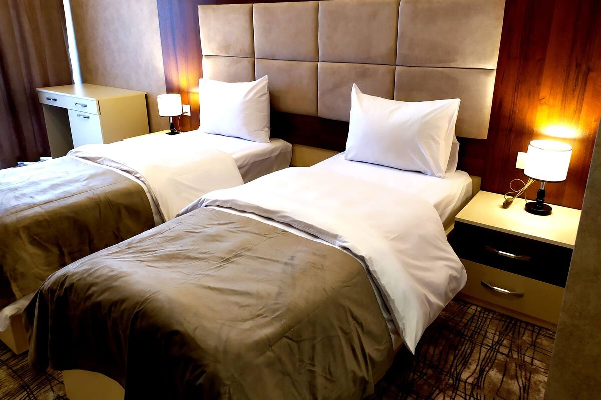 A hotel room with two beds, each with a nightstand, a lamp, and a drawer.