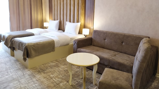 A hotel room with a large bed, two bedside tables, a sofa, and a small round table. - The Clocktower Hotel (Baku)