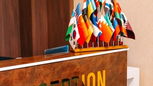 A reception desk with the word "RECEPTION" and multiple national flags displayed above it. - The Clocktower Hotel (Baku)