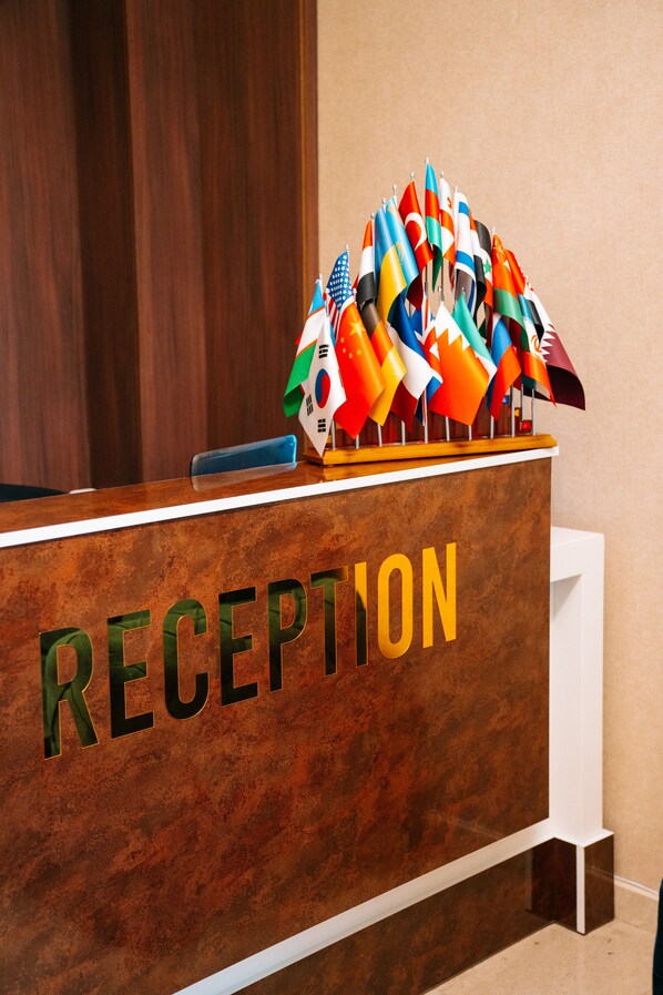 A reception desk with the word "RECEPTION" and multiple national flags displayed above it. - The Clocktower Hotel (Baku)